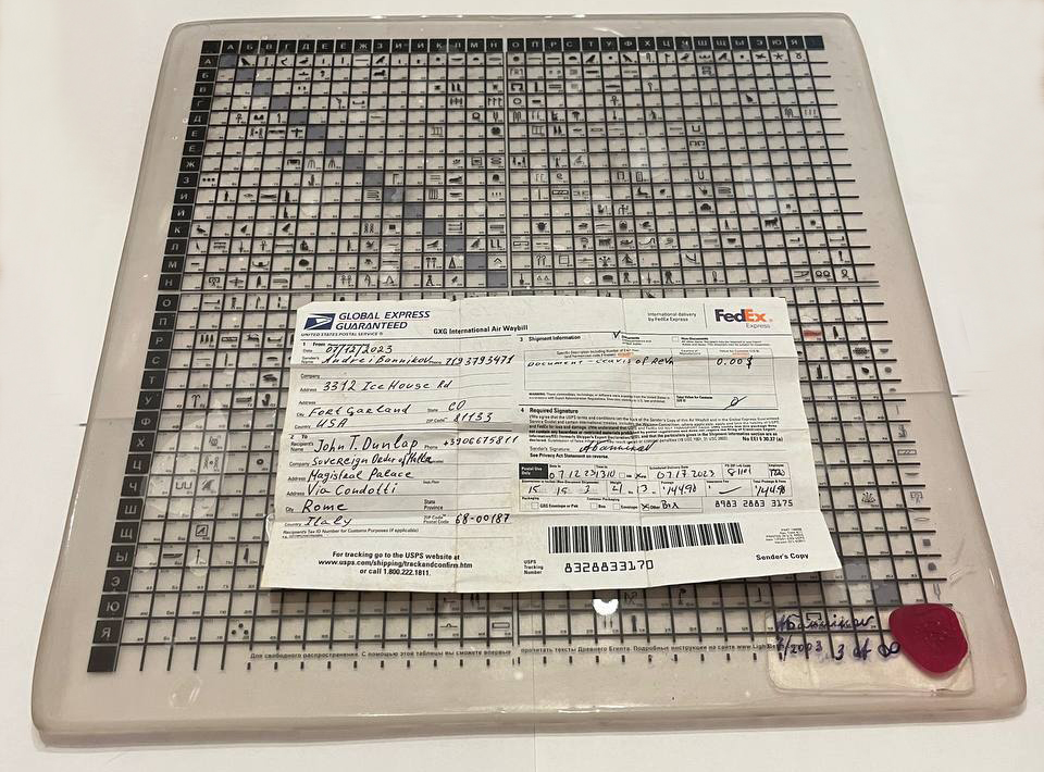 One of only two existing physical editions of Clavis of Revelation as it stood in July 2023. The transparent hieroglyphic matrix, encapsulated in clear epoxy resin, is shown together with the original FedEx shipping label addressed to Fra’ John T. Dunlap, Prince and Grand Master of the Sovereign Military Hospitaller Order of Saint John of Jerusalem, of Rhodes and of Malta.